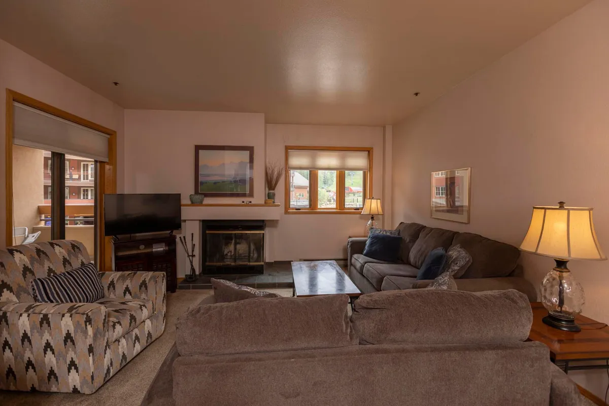 A welcoming living area anchored by a fireplace, with plush sofas and a coffee table set in front of large windows. The space offers both an inviting spot for relaxation and an additional sleeping option via the sleeper sofa, ideal for families or groups.