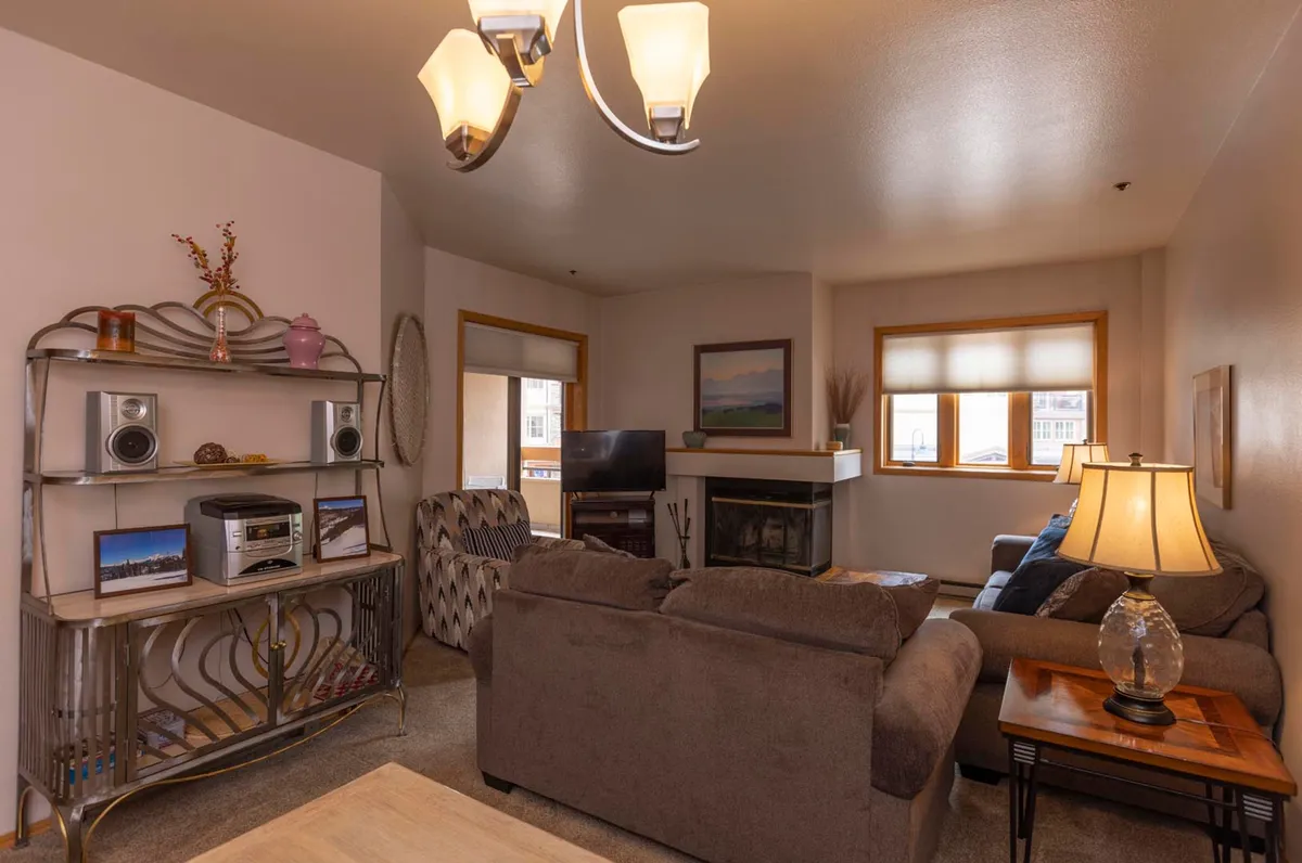 This image shows a welcoming living room with a comfortable sofa positioned near a wood-burning fireplace. The space is accented by a bookshelf, a lamp, and a TV, creating a relaxed and inviting atmosphere ideal for unwinding or socializing.