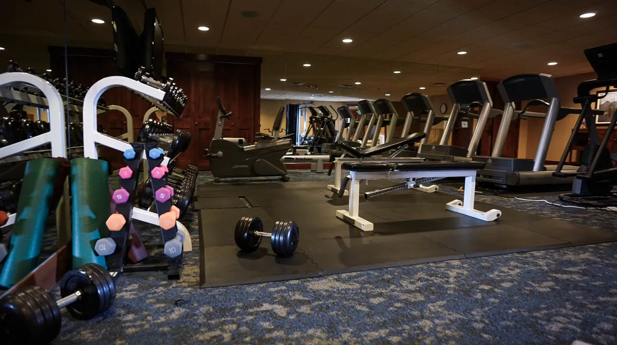 A modern, well-equipped fitness center featuring treadmills, dumbbells, and a weight bench, set in a bright, motivational space. It’s clear this amenity encourages guests to maintain their fitness routine or warm up for the day’s adventures.