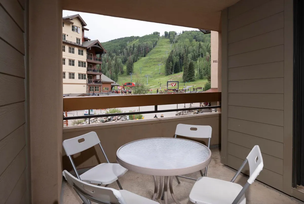 A cozy balcony seating area overlooks charming resort buildings and sweeping mountain vistas. The scene evokes a sense of casual comfort, ideal for enjoying a morning coffee, socializing after a day in the village, or simply soaking in the mountain atmosphere.