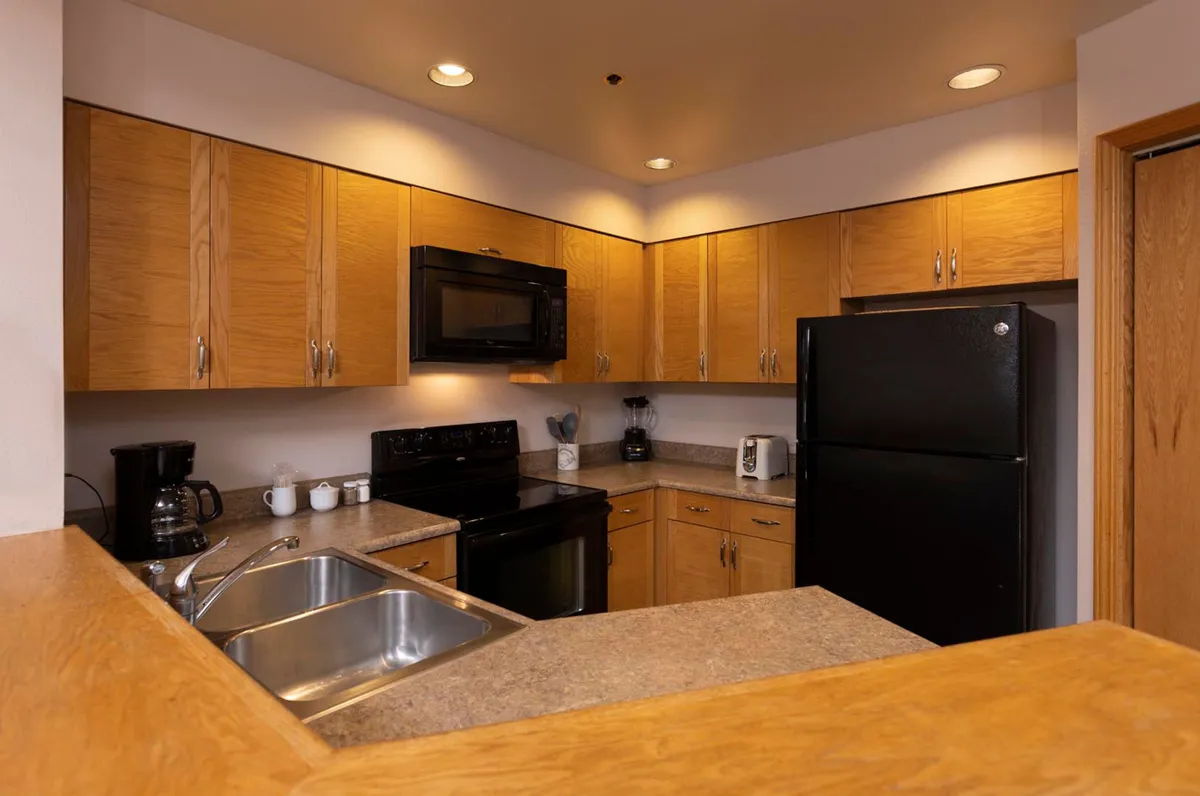 A cozy interior kitchen scene with warm wooden cabinetry, black appliances, ample counter space, and a sink. The atmosphere is inviting and practical, suggesting a comfortable home base for extended stays, meal preparation, and socializing.