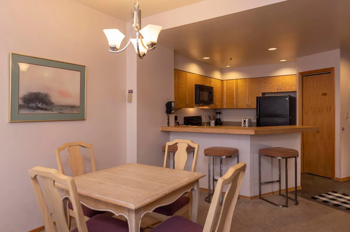 The image captures a cozy dining area adjacent to a kitchen counter, with a prominent dining table and bar stools. Framed artwork and soft lighting enhance the ambiance, making it ideal for family gatherings and shared meals.