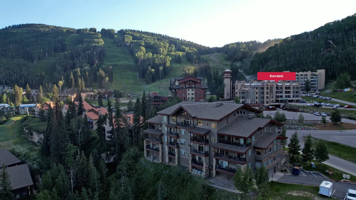 A sweeping exterior shot featuring resort buildings nestled against a majestic mountain backdrop. The image captures outdoor gathering spaces, a parking area for easy access, and the promise of sunrise adventures or evening gatherings by a communal fire pit—perfect for families seeking both excitement and connection.