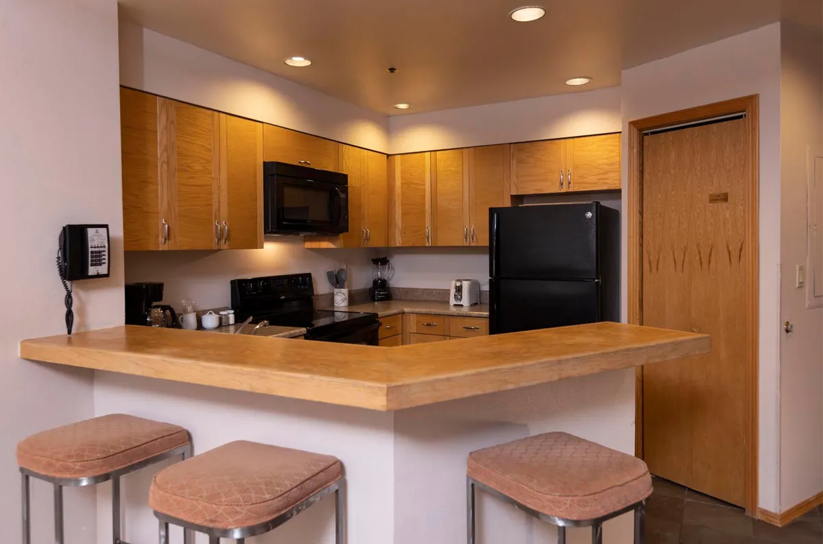 A view of the full kitchen featuring a kitchen island with bar stools, modern appliances, and wooden cabinetry. The space balances comfort and utility, providing a backdrop for cooking, casual dining, or entertaining.